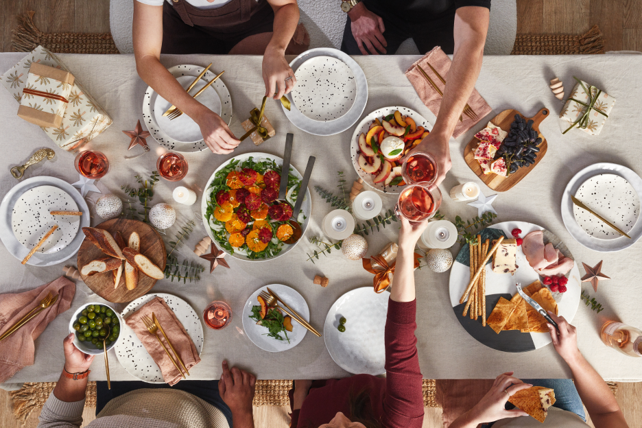 Top facing image of hands sharing food and drinks over a dining table with plates of Christmas lunch