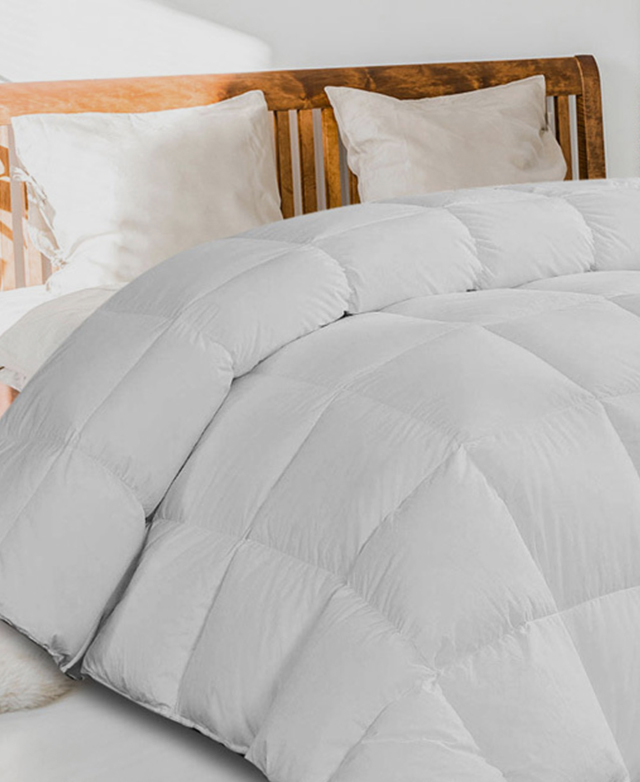 The all seasons quilt is styled on a wooden bed frame, illustrating its plush density and lofty baffle-box design.