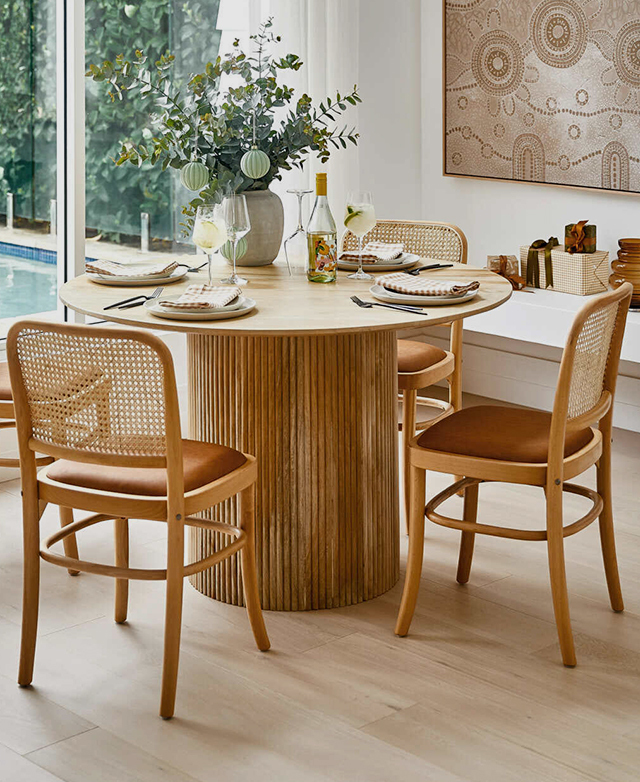 The dining chairs are positioned at a timber dining table with a fluted pedestal base, creating a warm and welcoming look.