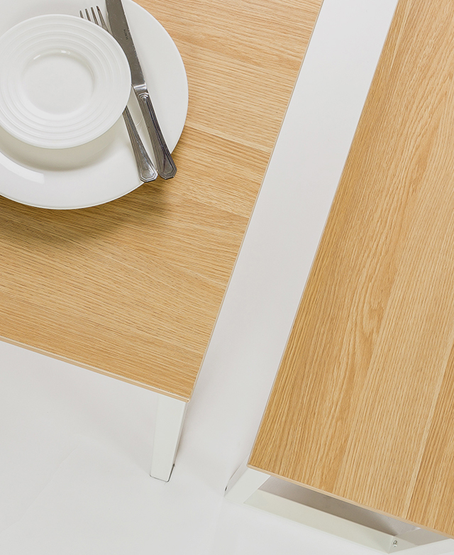 The table and one bench seat are viewed from above. A plate set, knife and fork rest on top of the table. The table and one bench seat are viewed from above. A plate set, knife and fork rest on top of the table.