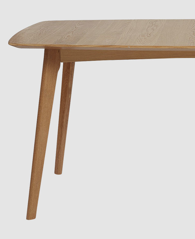 Half of the dining table is shown from a side angle, illustrating the smooth oak wood texture and bevelled table top edge. Half of the dining table is shown from a side angle, illustrating the smooth oak wood texture and bevelled table top edge.