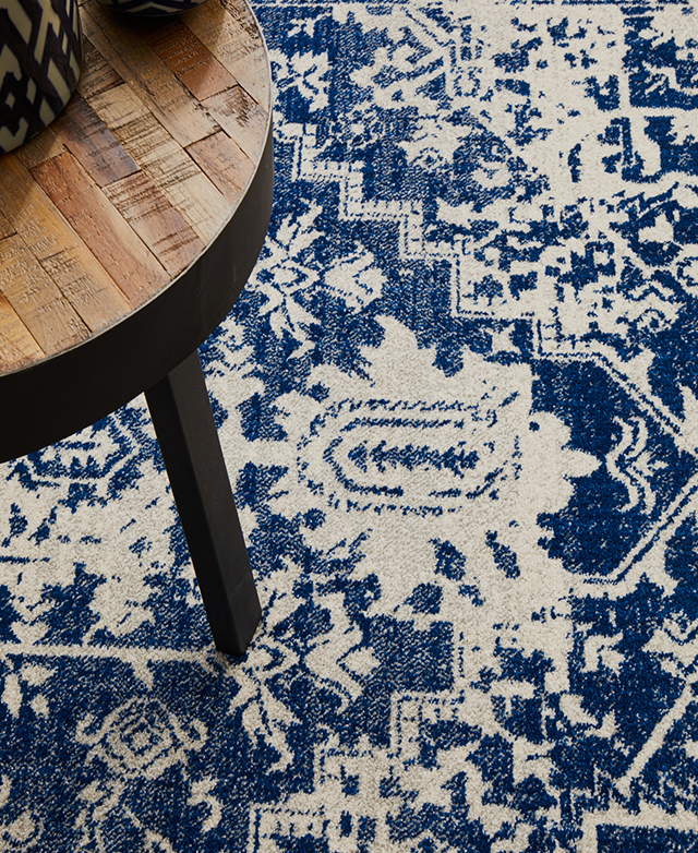 Close-up illustrates a rug's deep blue and cream colourway and traditional pattern. It sits underneath a timber coffee table.