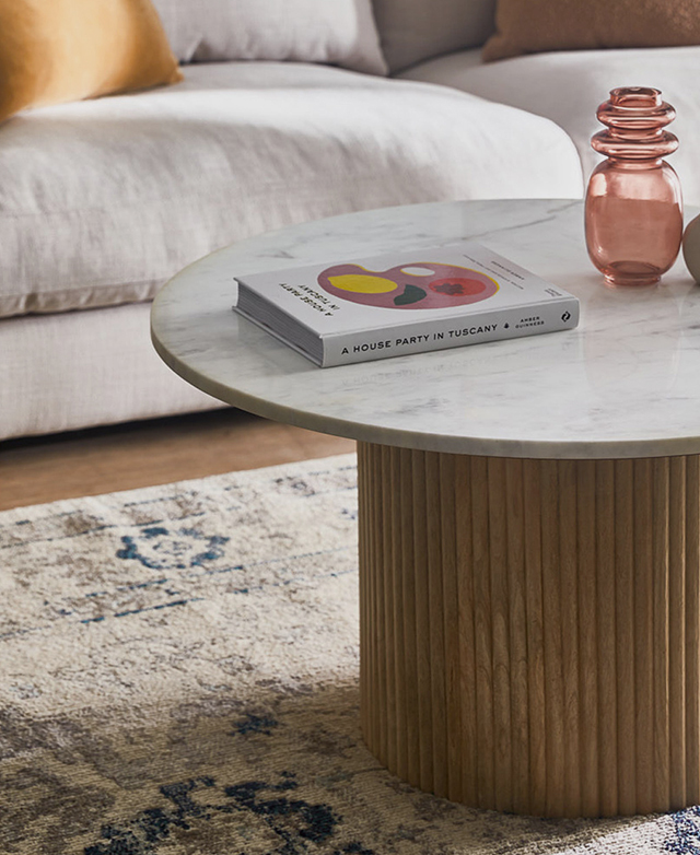 A marble and mango wood coffee table in situ, with a book and a pink decorative glass vase styled on top.