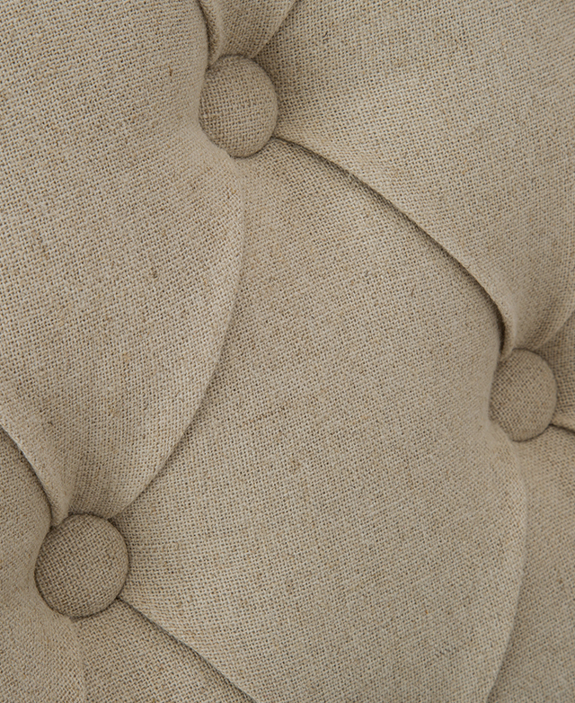 Close-up of diamond button tufting on an armless dining chair upholstered in a beige linen-blend fabric. Close-up of diamond button tufting on an armless dining chair upholstered in a beige linen-blend fabric.