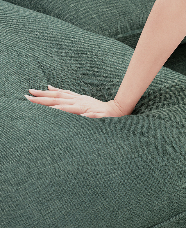 A hand presses down on a yielding sofa cushion with blue-green polyester upholstery. A hand presses down on a yielding sofa cushion with blue-green polyester upholstery.