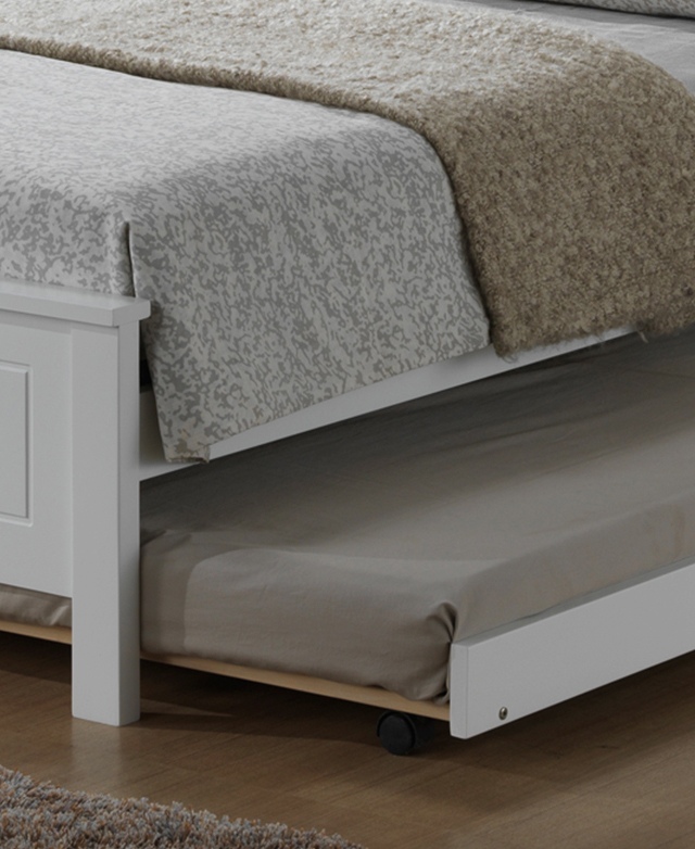 A trundle with castor wheels is slightly pulled out from underneath a white bed frame.