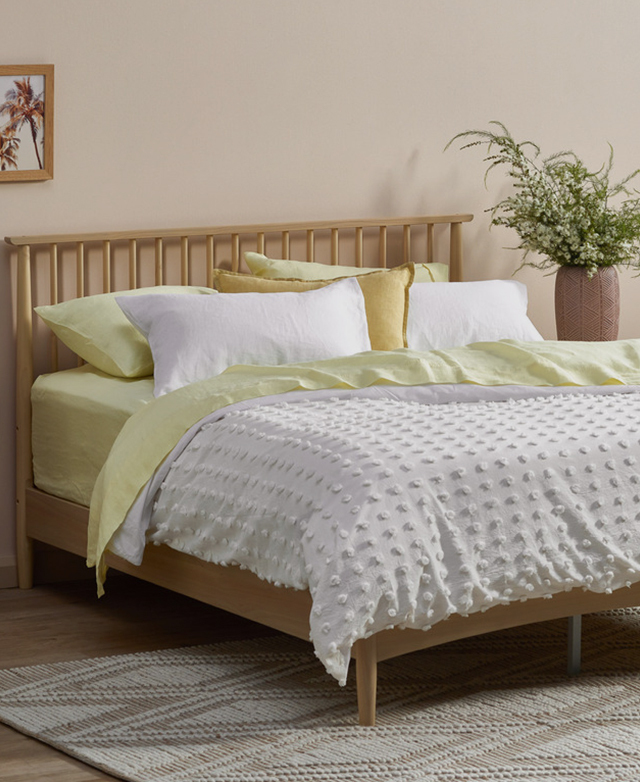 A tufted white quilt cover and lemon sheets dress the bed. The bedhead is flush against a peachy wall.