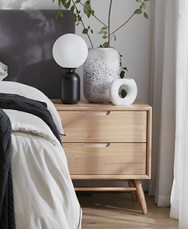 A timber bedside table styled with black and white decorative accents in a contemporary bedroom space.
