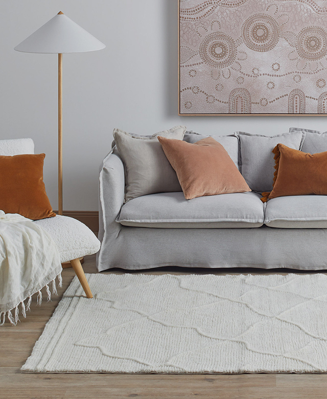 In a contemporary living space, a white wool rug is styled on top of timber flooring in front of a grey linen sofa. In a contemporary living space, a white wool rug is styled on top of timber flooring in front of a grey linen sofa.