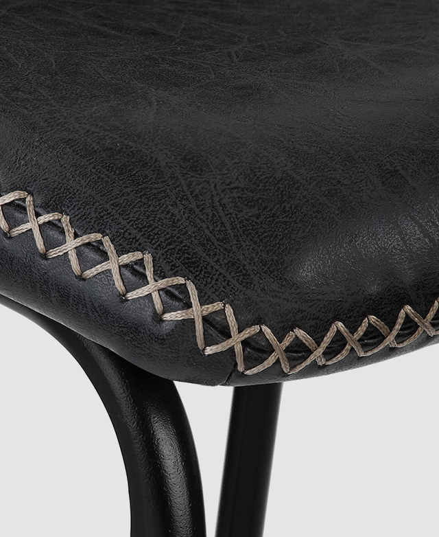 Large-scale view of a corner of the barstool's seat. It's covered in black faux leather upholstery, with a distinctive cross-stitch where the fabric joins together.