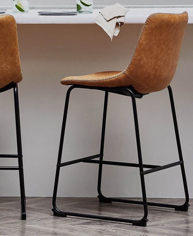 Two tan barstools are positioned at a kitchen counter, one is at an angle. Two drinks and a napkin are on the table top.