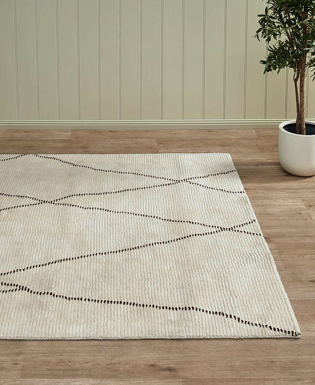 A neutral rug with an abstract linework pattern is styled above timber flooring.