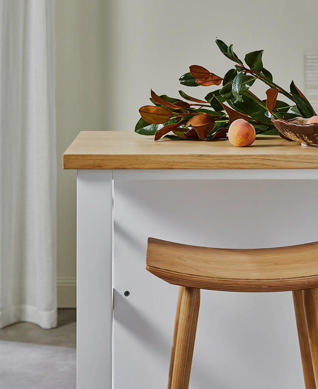 The timber barstool is tucked underneath a timber and white kitchen island bench, illustrating its compact profile. The timber barstool is tucked underneath a timber and white kitchen island bench, illustrating its compact profile.