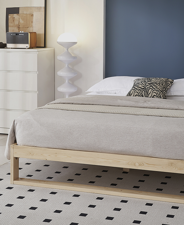 A wooden bed frame with a mattress on top. It's neatly styled with beige bedding.