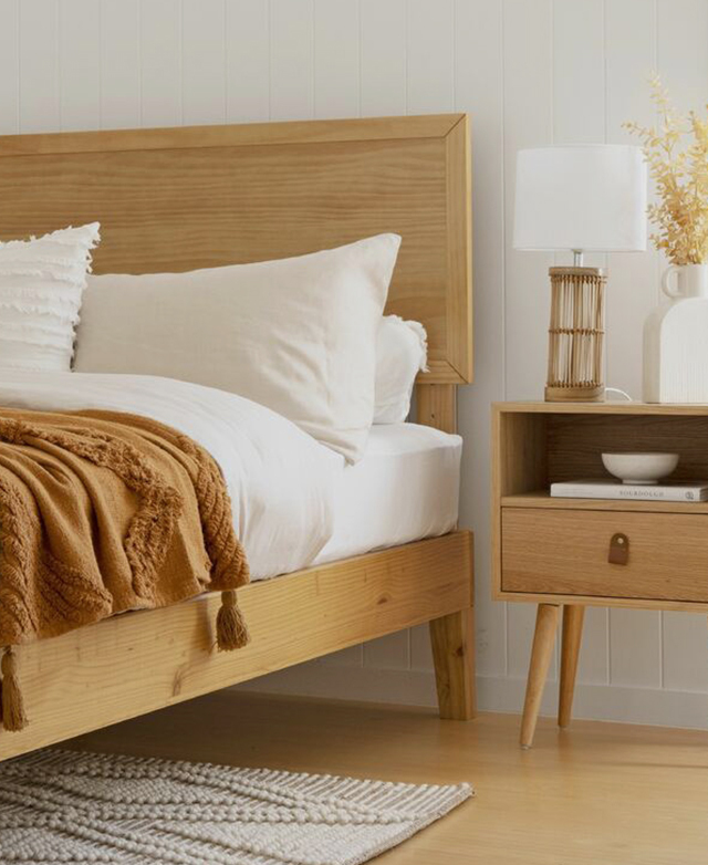 The honey pine wood bed frame is complemented by an adjacent matching wooden bedside table.
