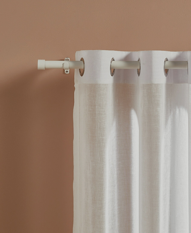 A white sheer eyelet curtain is styled on a slender white curtain rod with simple finials at the end.