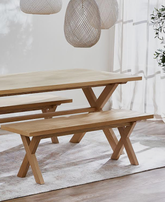 A matching timber dining table and pair of timber benches styled underneath hanging pendant lights in a bright space.