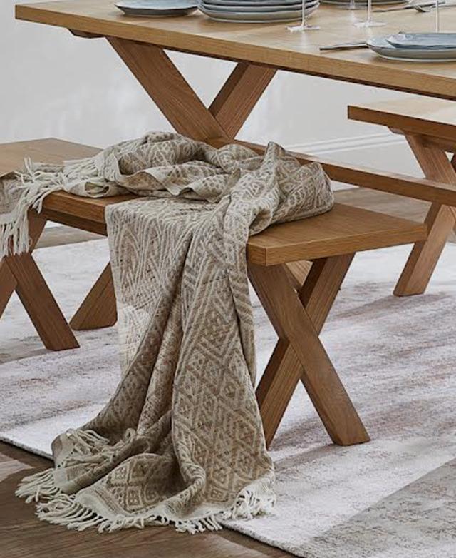 A simple timber dining bench has a beige throw with a geometric print draped over the top.