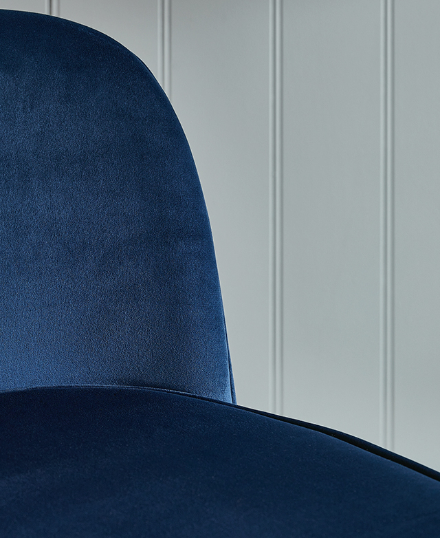 The seat of an office chair with rich blue velvet upholstery and neat piping trims around the seat and backrest.