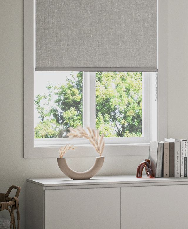A light grey fabric roller blind is partially open, filtering light from entering a home.