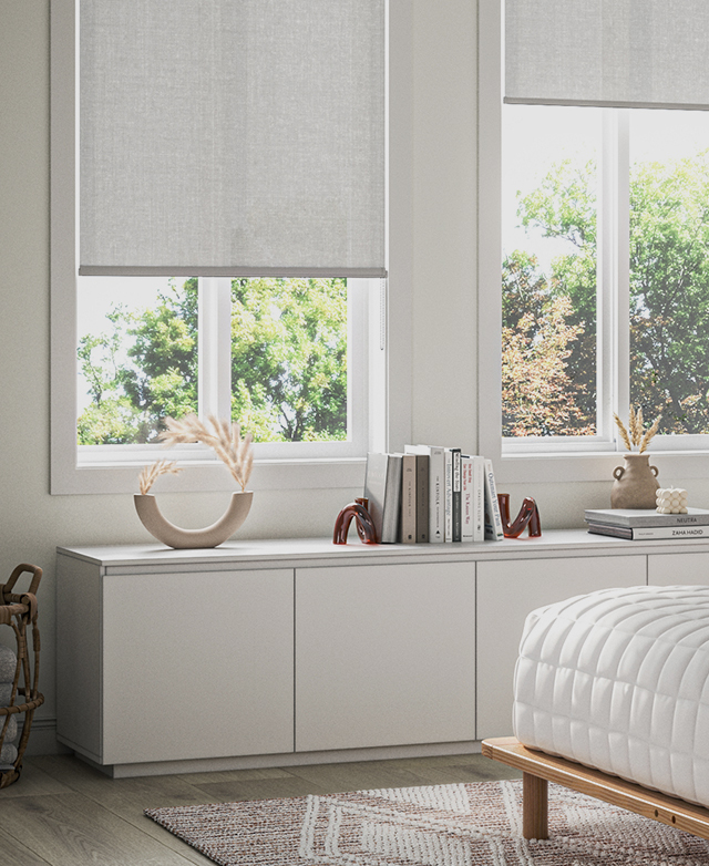 Light filters through the shade of a sand-coloured fabric roller blind into a bedroom space.