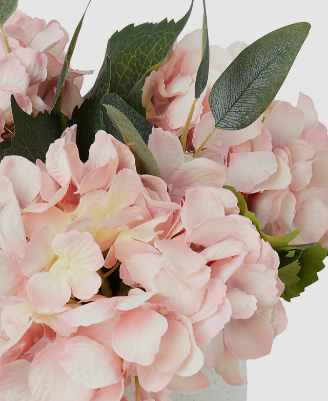 A faux hydrangea flower with soft pink petals and green leaves.