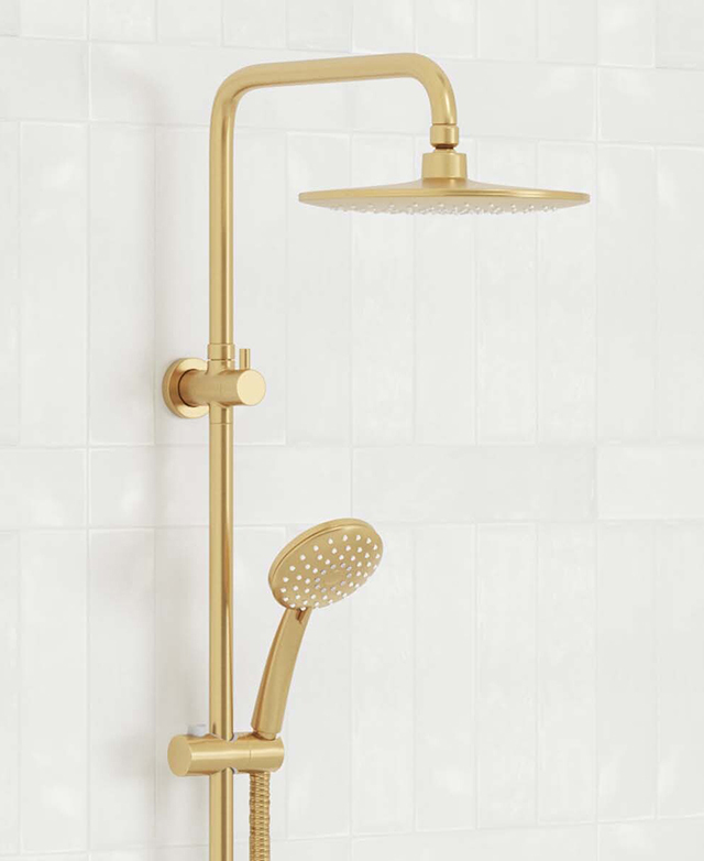 Top half of a gold twin shower mounted on a white tile wall