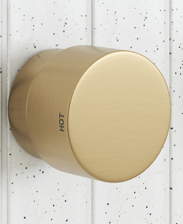 wall mounted brushed gold dial style tapware showing the hot indicator on the dial with a speckled tile background