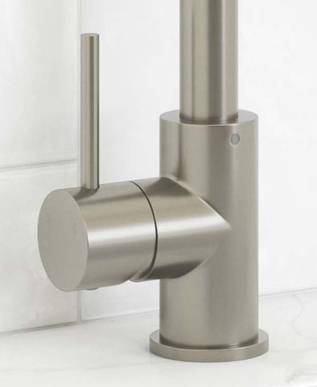 Base with lever of the Clovelly brushed nickel kitchen sink mixer on a benchtop in front of a tiled wall. Base with lever of the Clovelly brushed nickel kitchen sink mixer on a benchtop in front of a tiled wall.