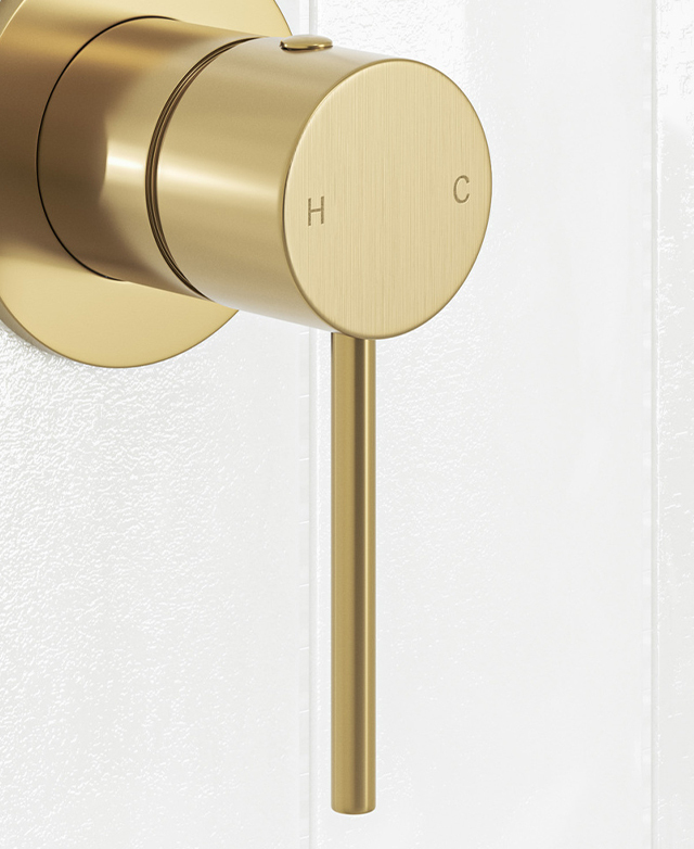 Close-up of brushed gold shower/bath wall mixer with pin lever mounted on a white tiled wall