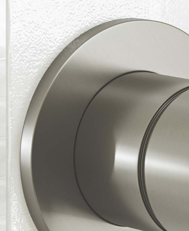 Close-up of top left corner of the round brushed nickel backplate against a white tiled wall