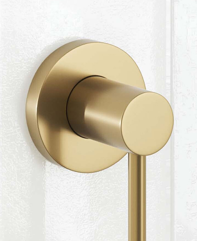 Close-up of the clovelly brushed gold round backplate and part of the robe hook on a white tiled wall Close-up of the clovelly brushed gold round backplate and part of the robe hook on a white tiled wall