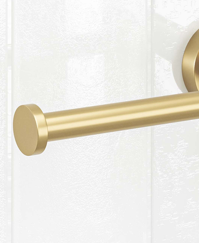 Close-up of end part of the holder of the left-facing brushed gold toilet roll holder before a white tiled wall