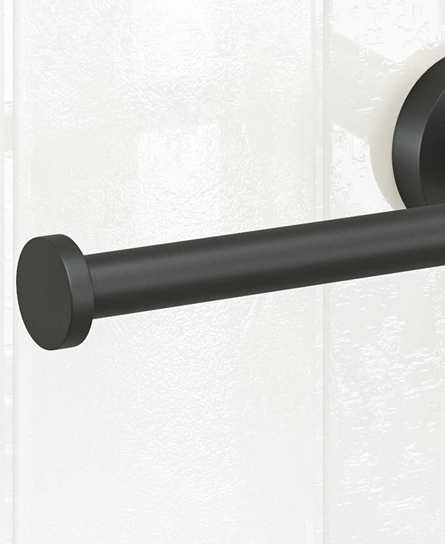 Close-up of the matte black toilet roll holder part before a white tiled wall