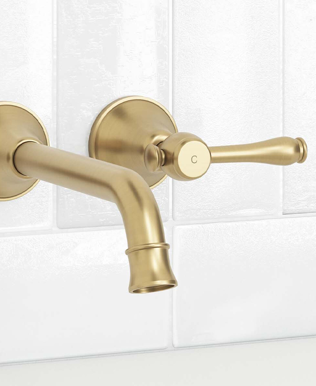 Close-up of the stanwell brushed gold wall mixer spout and one lever tap for cold water against a white tiled wall