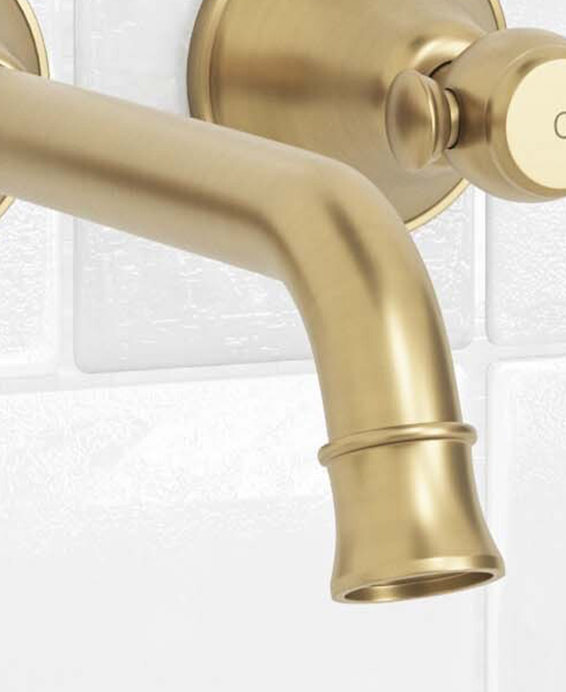 In-depth close-up of the brushed gold spout and part of the round backplate of the lever tap against a white tiled wall