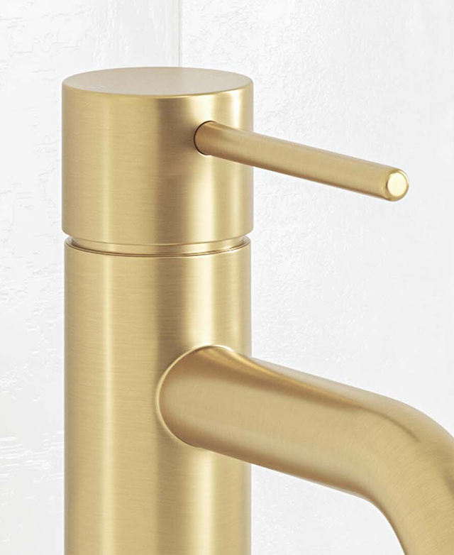 Close-up of the top part of the clovelly brushed gold mixer with pin lever, body and part of spout in front of a white tiled wall