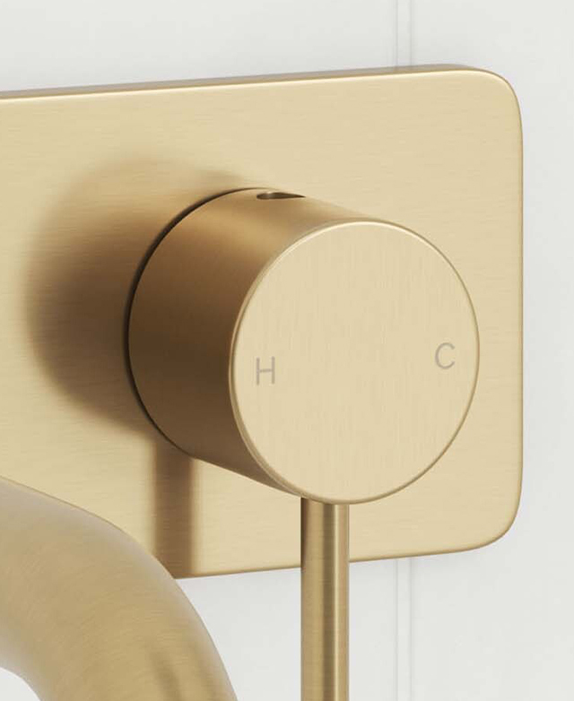 Close-up of brushed gold wall mixer with 'H' and 'C' temperature indicators and the rectangular backplate