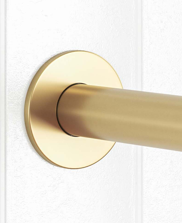 Close-up of the brushed gold round backplate and part of the round spout mounted on a white tiled wall