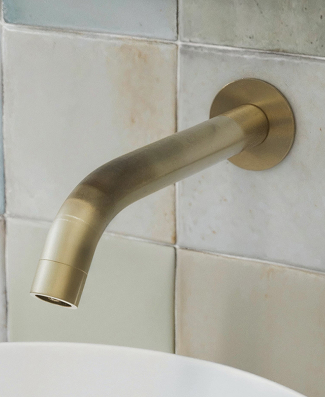 Clovelly brushed gold wall spout mounted on tiled wall above a round basin