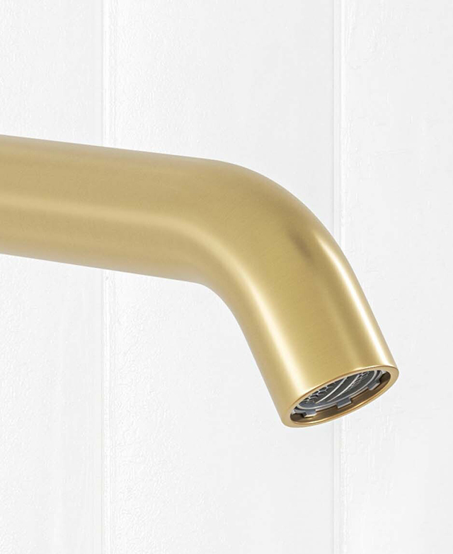 Close-up of the curved brushed gold round spout in front of a white tiled wall