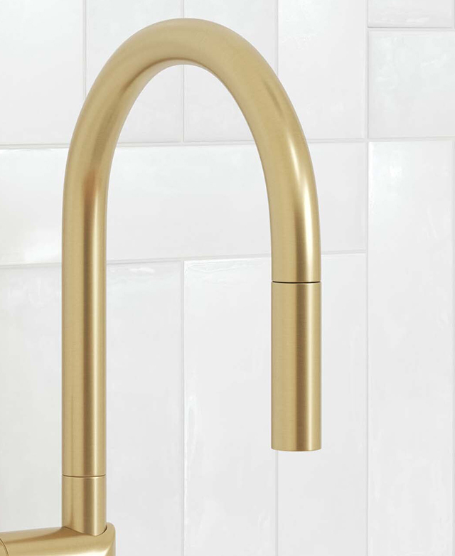 Close-up of the brushed gold gooseneck with pull-out nozzle in front of a white tiled wall