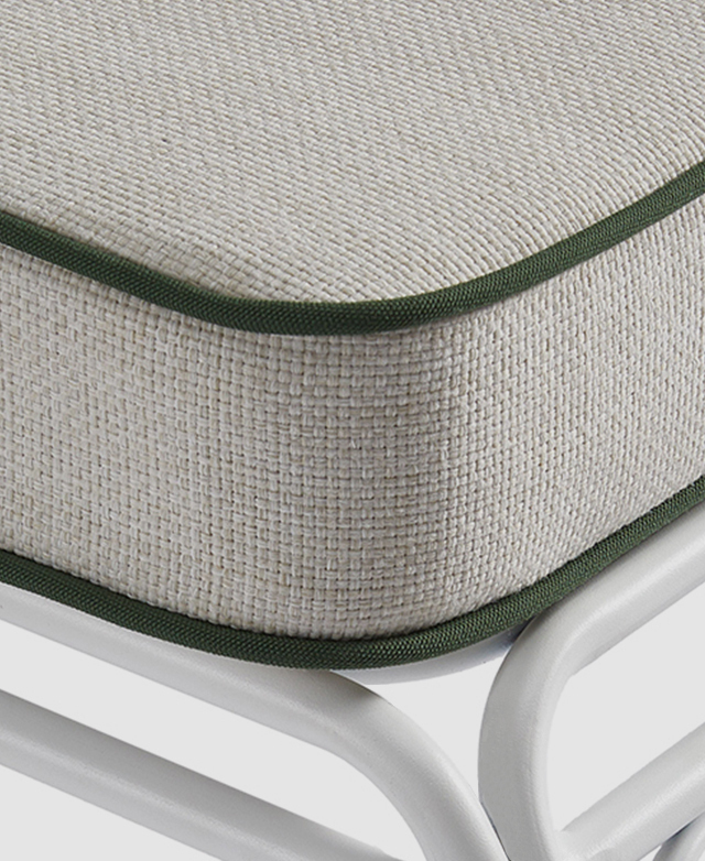 A rounded front corner of the off-white cushion with green piping trims. A rounded front corner of the off-white cushion with green piping trims.