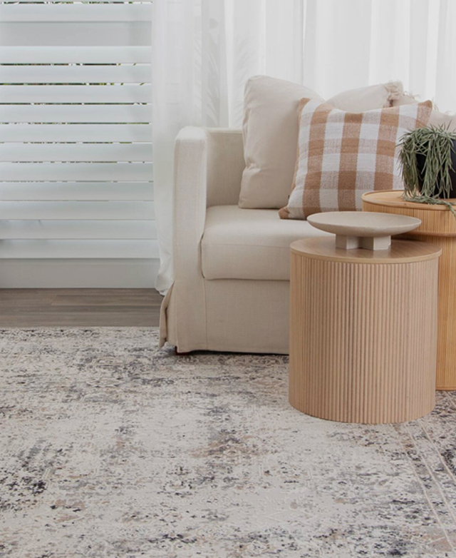 A grey velvet tub chair and polished side table with foliage on top are placed on top of the rug. A grey velvet tub chair and polished side table with foliage on top are placed on top of the rug.