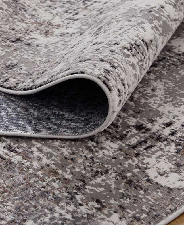 The grey polypropylene rug is partially rolled up on the floor. The grey polypropylene rug is partially rolled up on the floor.