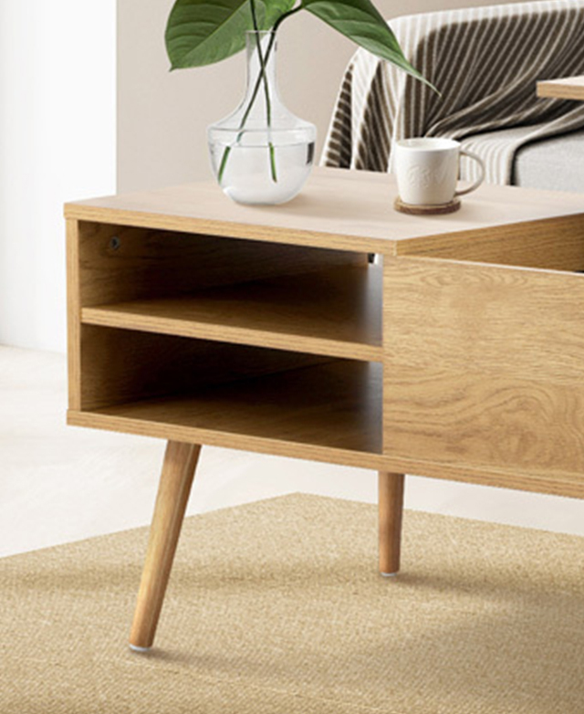 One end of the coffee table is shown; it's on a flatweave sand rug, and on top is a vase of green leaves and a white mug.
