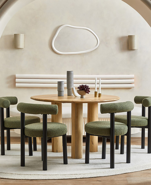 Four green boucle dining chairs are positioned around a round timber dining table in a beautiful neutral setting.