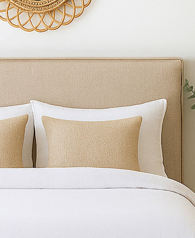 A cropped, front-facing view of a warm, neutral-toned bedhead against a white wall.