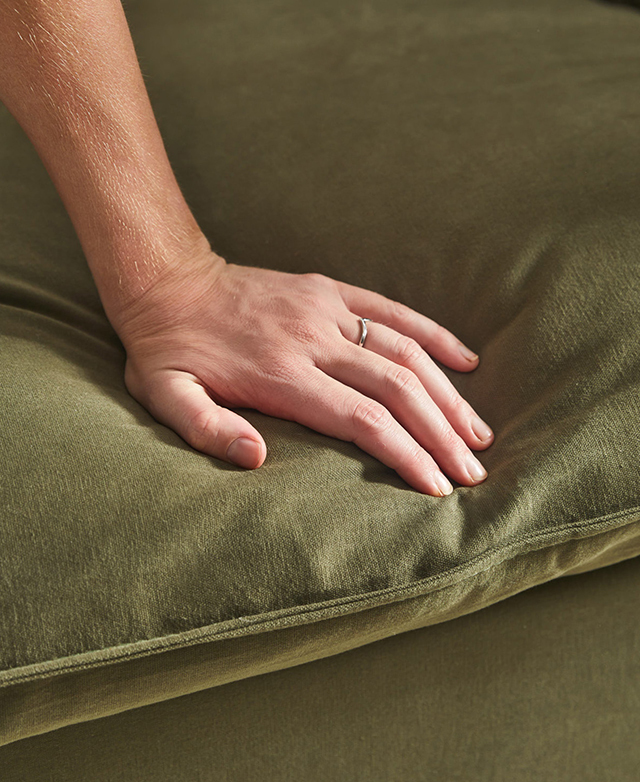A hand is shown pushing into the green sofa.