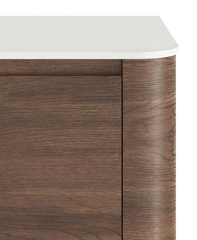 A rounded front corner of the white sintered stone vanity top is above an oak-coloured body.